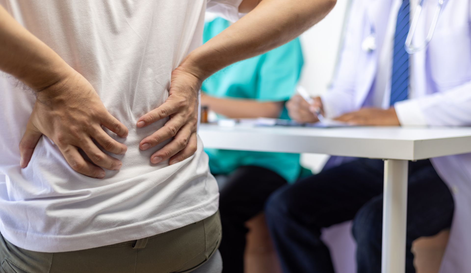 A man is holding his back in pain while a doctor looks on in Guelph, ON