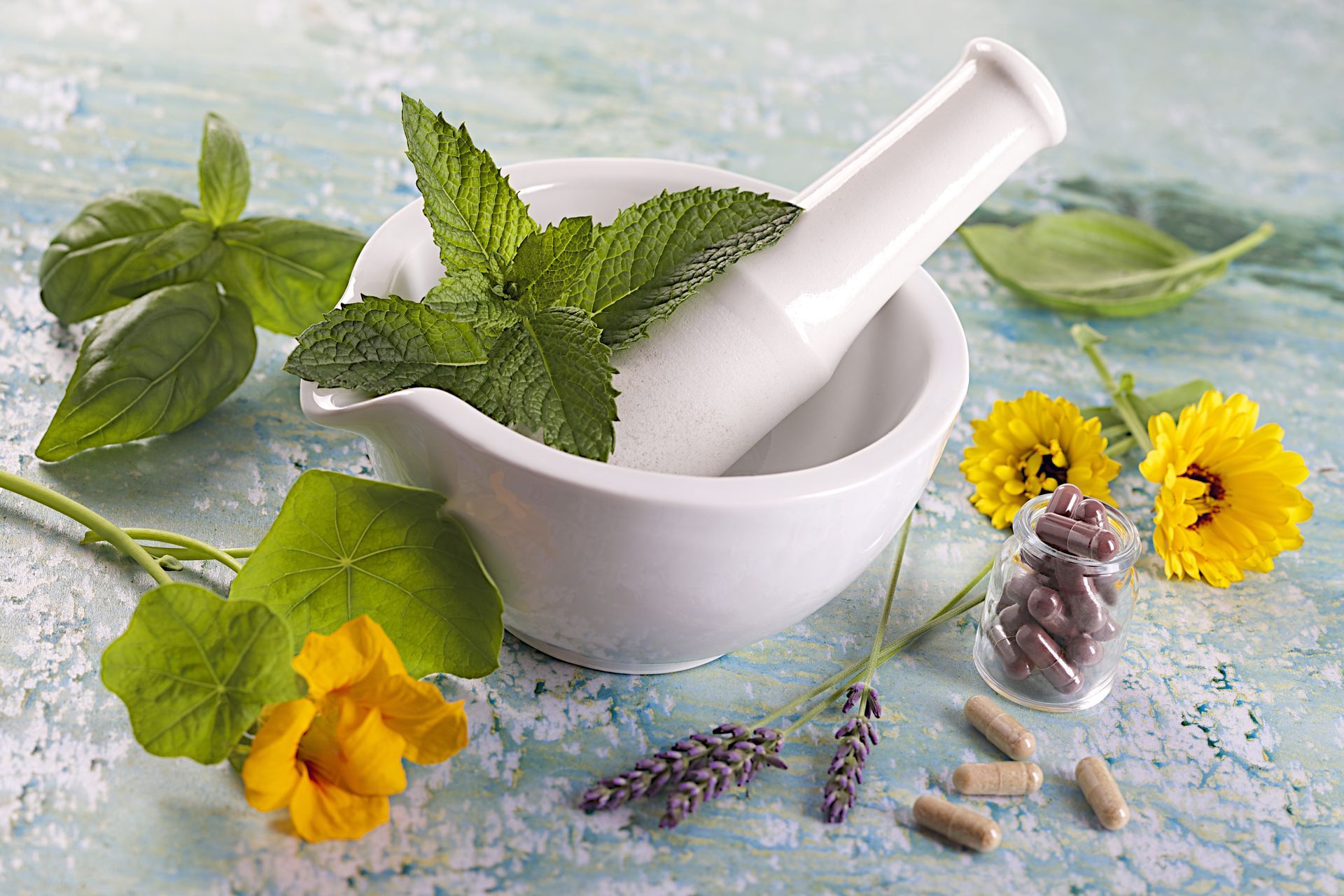 A mortar and pestle with mint leaves and flowers on a table.
