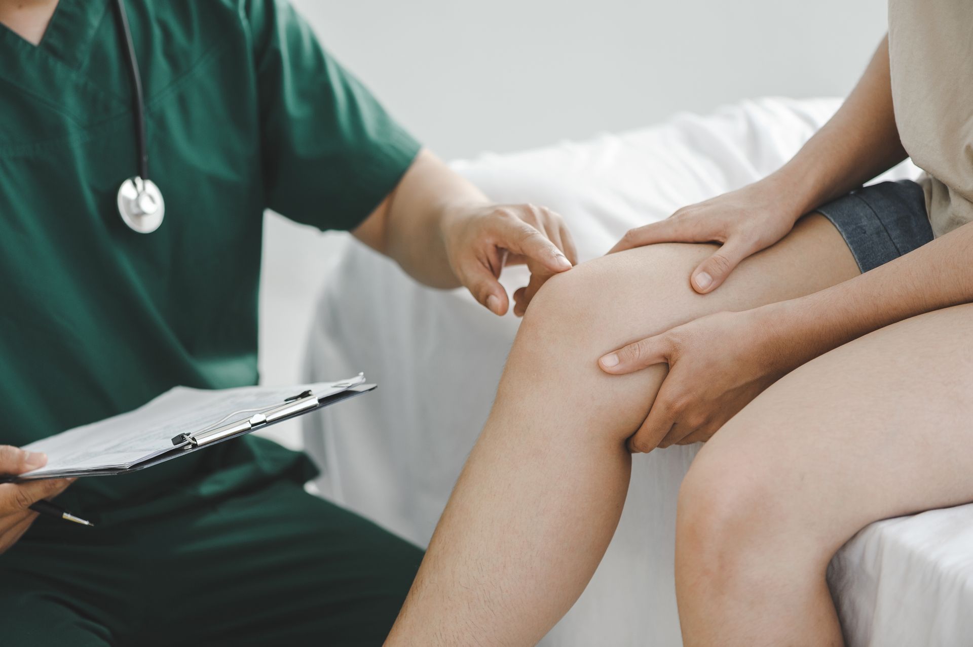 A doctor is examining a patient 's knee while holding a clipboard in Guelph, ON.