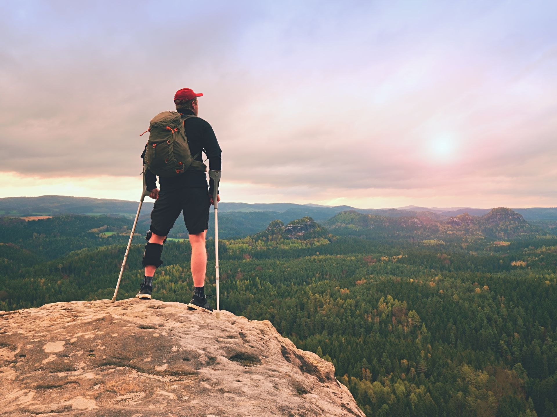 A man with a backpack and crutches is standing on top of a mountain in Guelph, ON