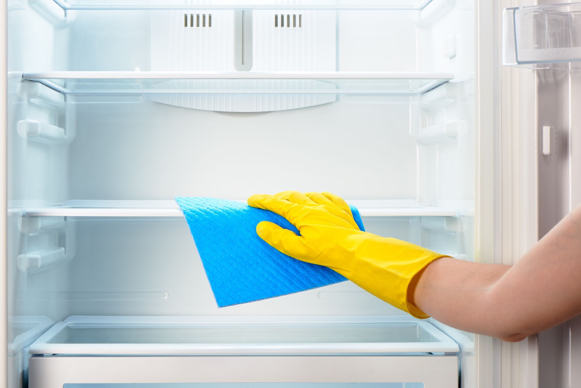 Cleaning an empty refrigerator with a blue cloth.
