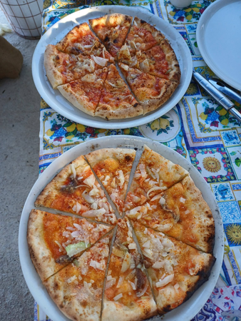 Due pizze su piatti bianchi, adagiate su una colorata tovaglia da esterno, tagliate a fette e pronte da mangiare.