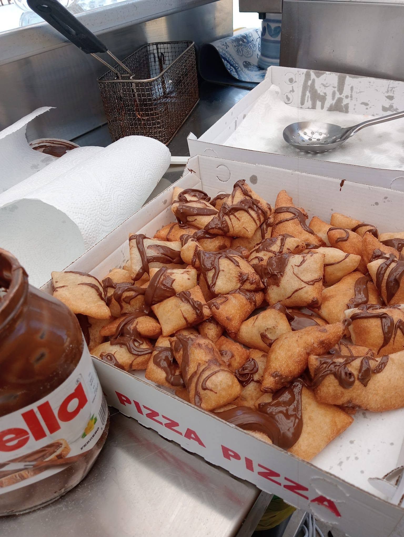 Una scatola di pasticcini fritti accanto a un barattolo di Nutella sul bancone della cucina.