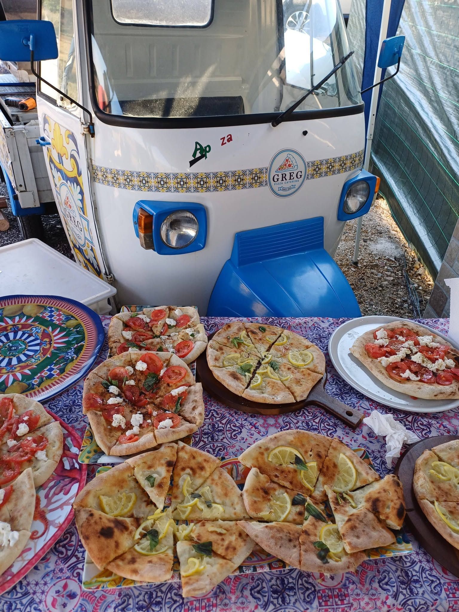 Piccolo furgoncino bianco per la vendita di cibo, con decorazioni a mosaico colorate e vassoi di fette di pizza sul davanti.
