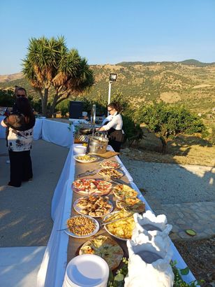 Un buffet all'aperto con diverse pietanze, allestito accanto a un punto panoramico sulla collina al tramonto.