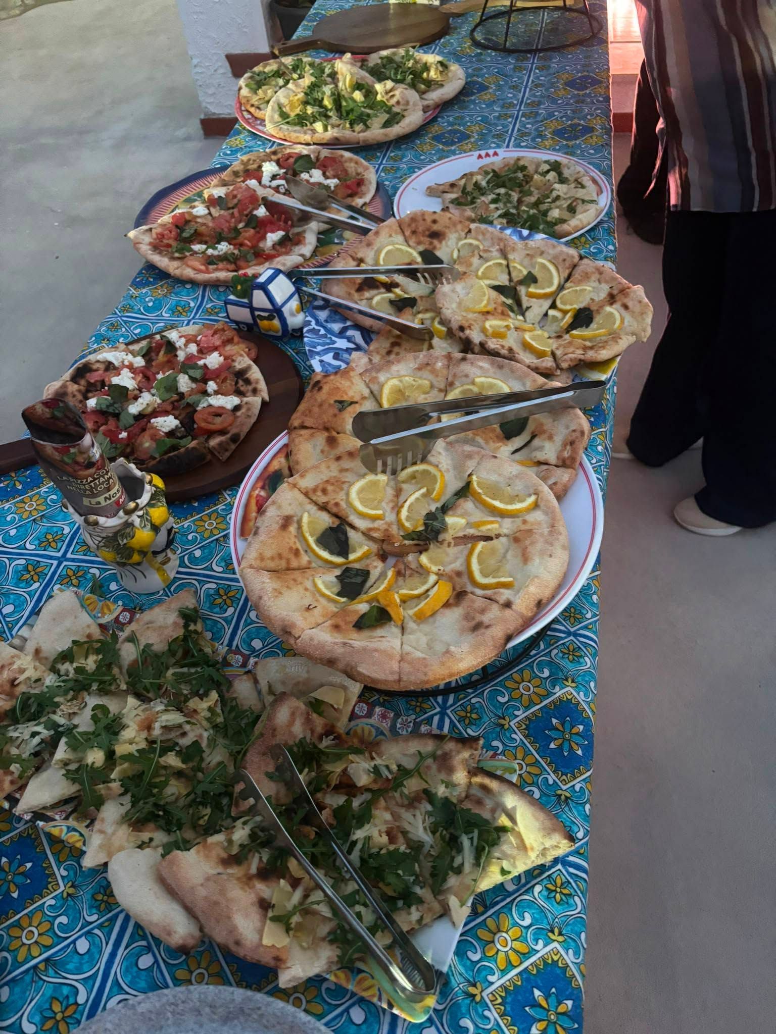 Un assortimento di pizze e focacce salate è esposto su una tovaglia blu in un buffet all'aperto.