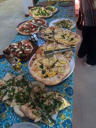 Diverse pizze e focacce su una tovaglia blu a motivi geometrici, in un buffet all'aperto.