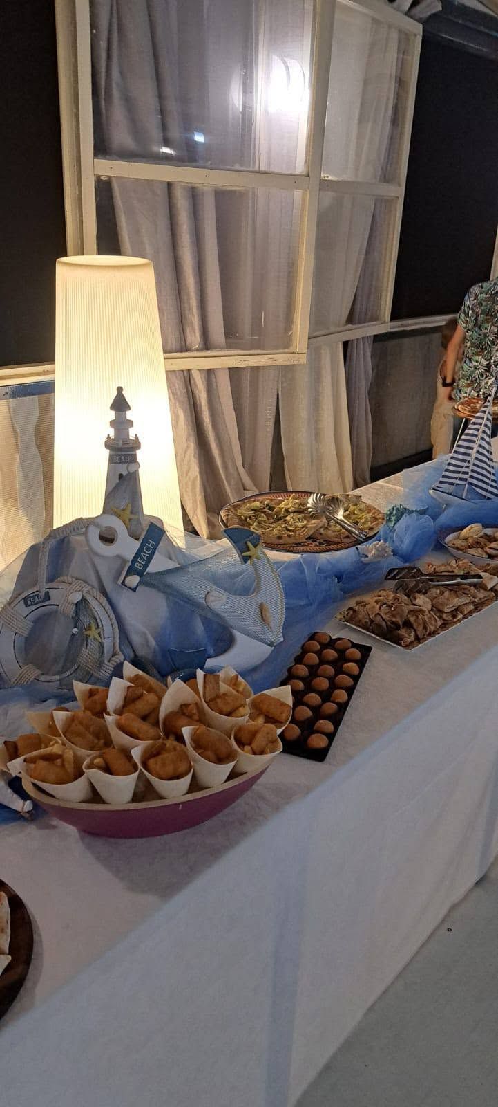 Tavolo dei dolci con pasticcini, cioccolatini e una lampada accesa accanto a una finestra di notte.