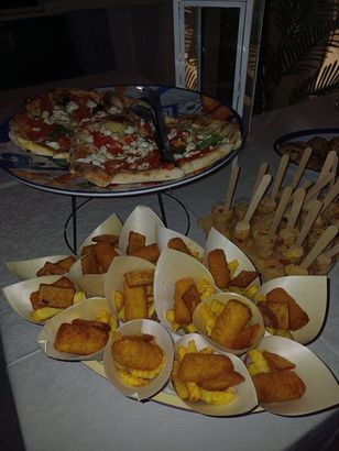 Su un tavolo, un vassoio con stuzzichini e fette di pizza, e sullo sfondo dei grissini.