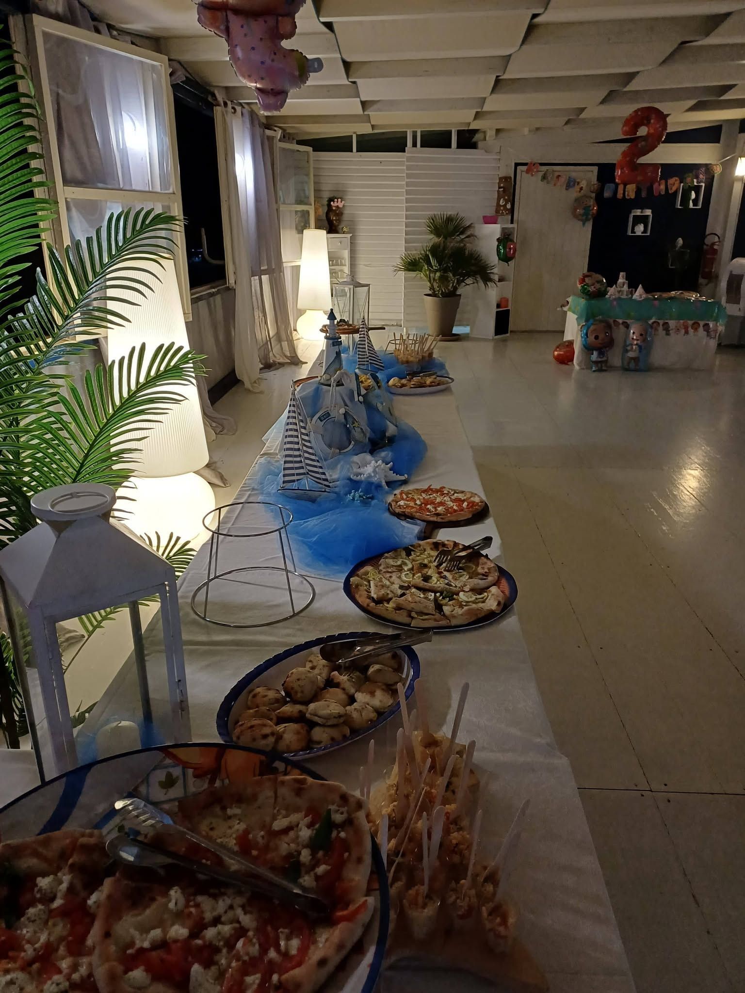 Tavolo da buffet con piatti e decorazioni floreali in una luminosa sala interna.