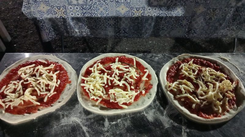 Tre ciotoline di salsa rossa con formaggio grattugiato su un piano di lavoro.