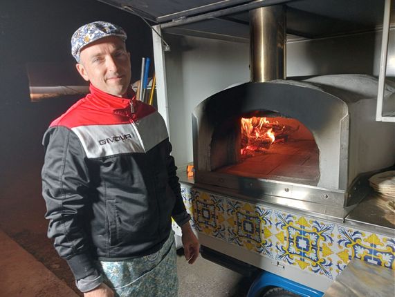 Persona in piedi accanto a un forno a legna con fuoco acceso e base decorata con piastrelle.