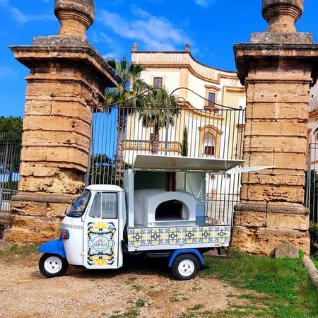 Un piccolo triciclo decorato blu e bianco parcheggiato davanti a un cancello di pietra e a un edificio storico