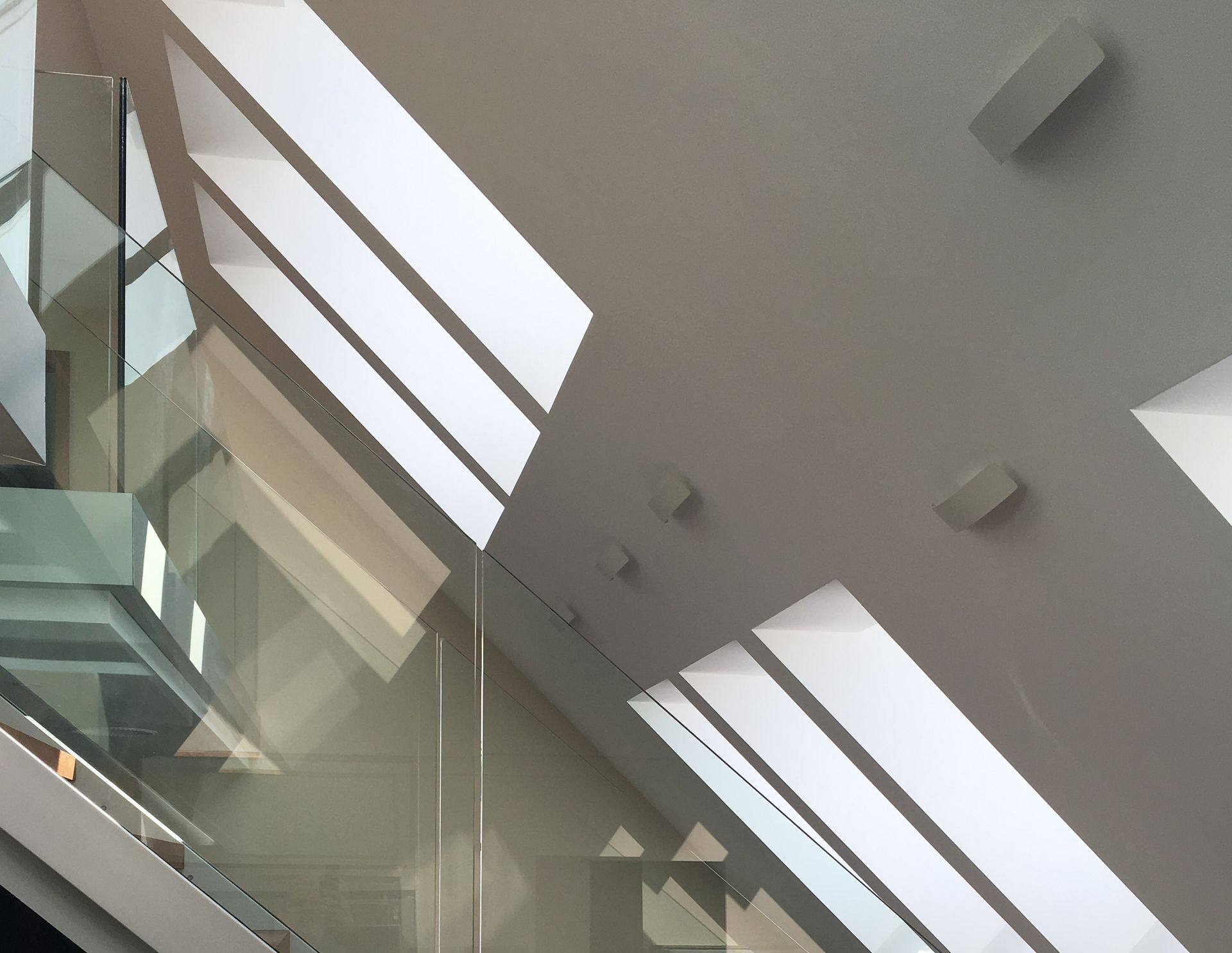 Geometrische Schatten von Fenstern auf einer weißen Decke und einer Glaswand. Einige Lautsprecher sind zu sehen.