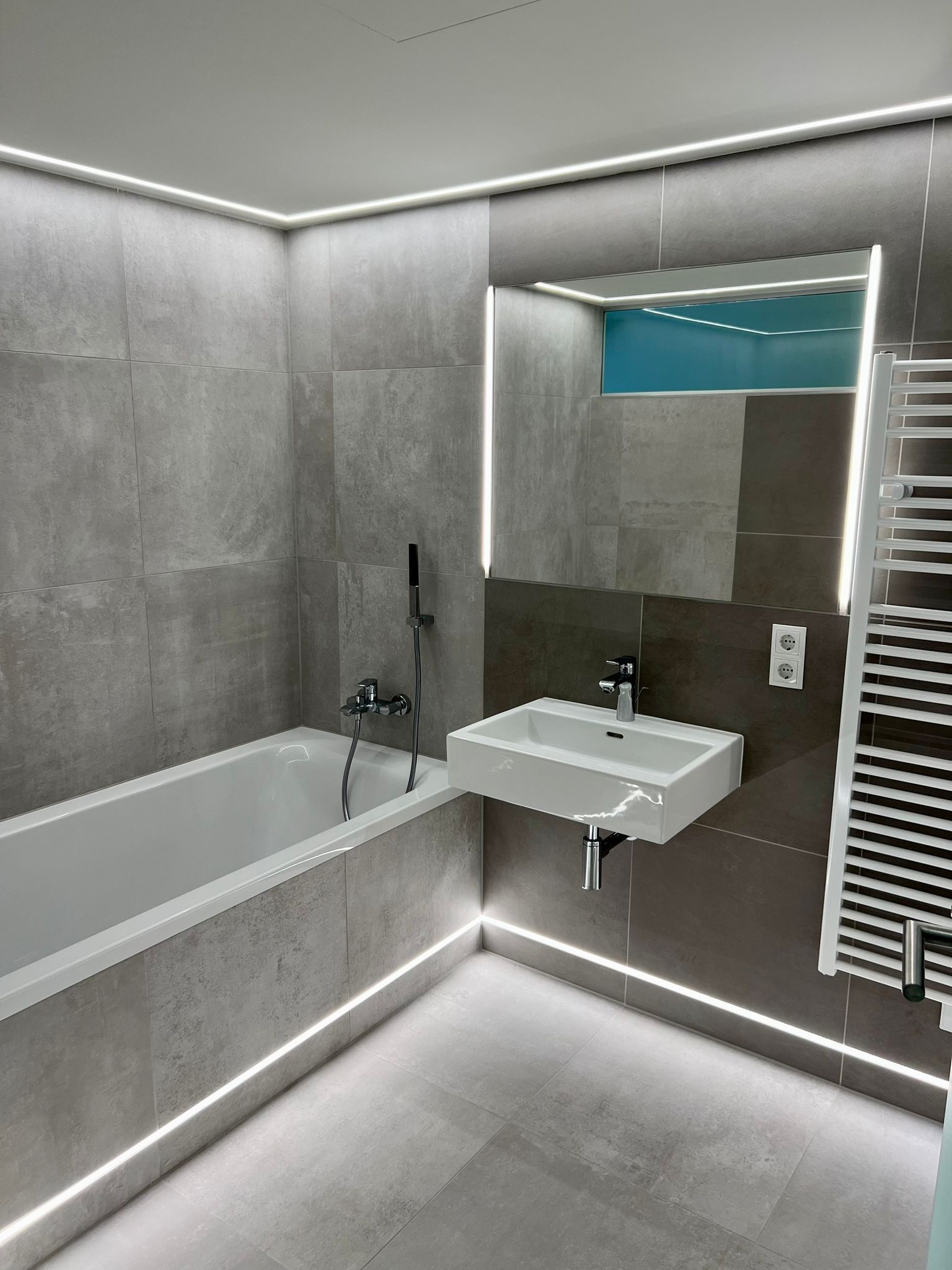 Modernes Badezimmer mit grau gefliesten Wänden, Badewanne, Waschbecken und beheiztem Handtuchhalter