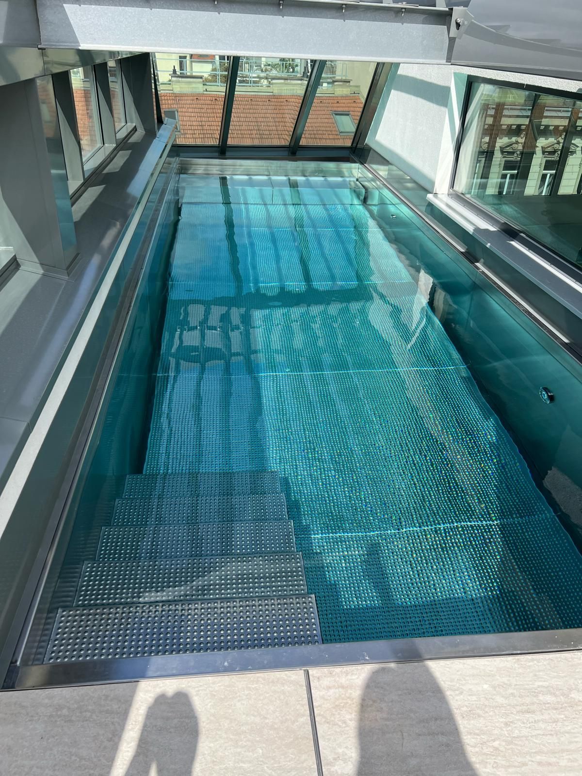 Schwimmbad auf dem Dach mit blauem Wasser und Metalltreppe unter einem Glasdach.