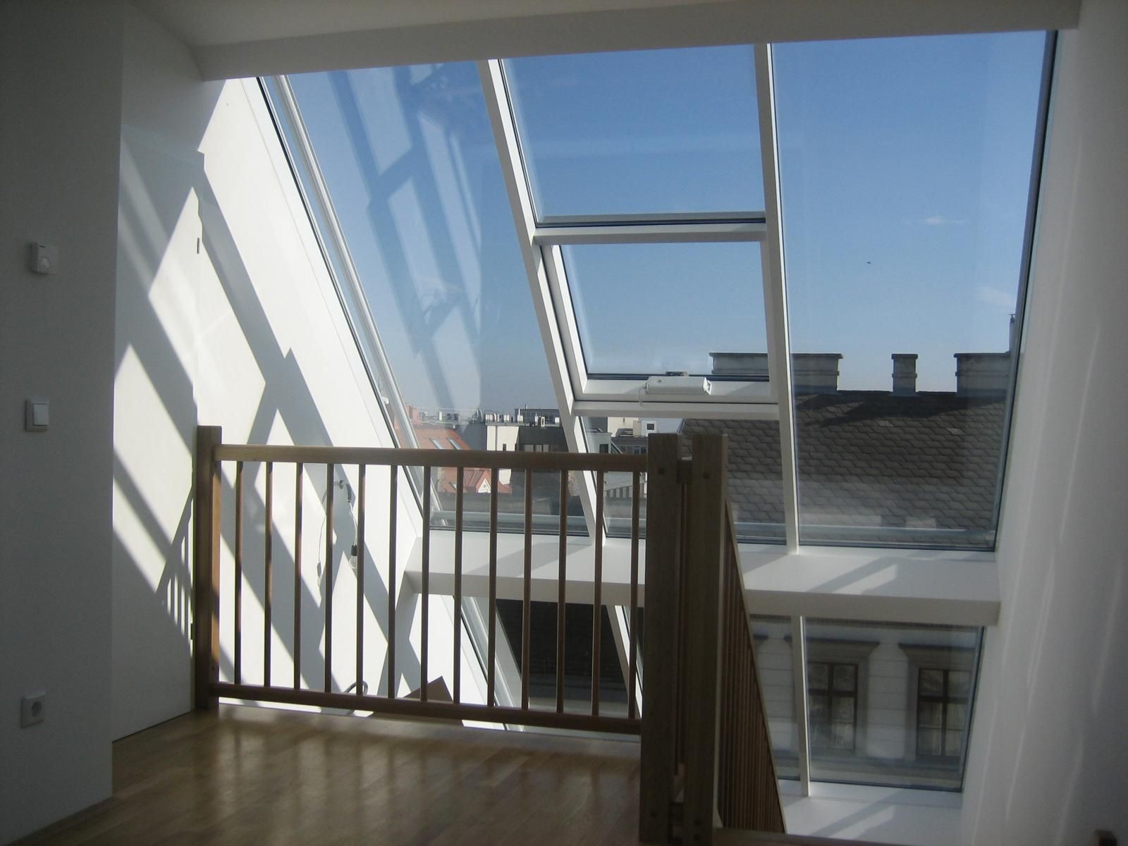 Innenansicht: Holzgeländer und Treppe, die zu einem großen Glasdachfenster mit Blick auf die Stadt führen.