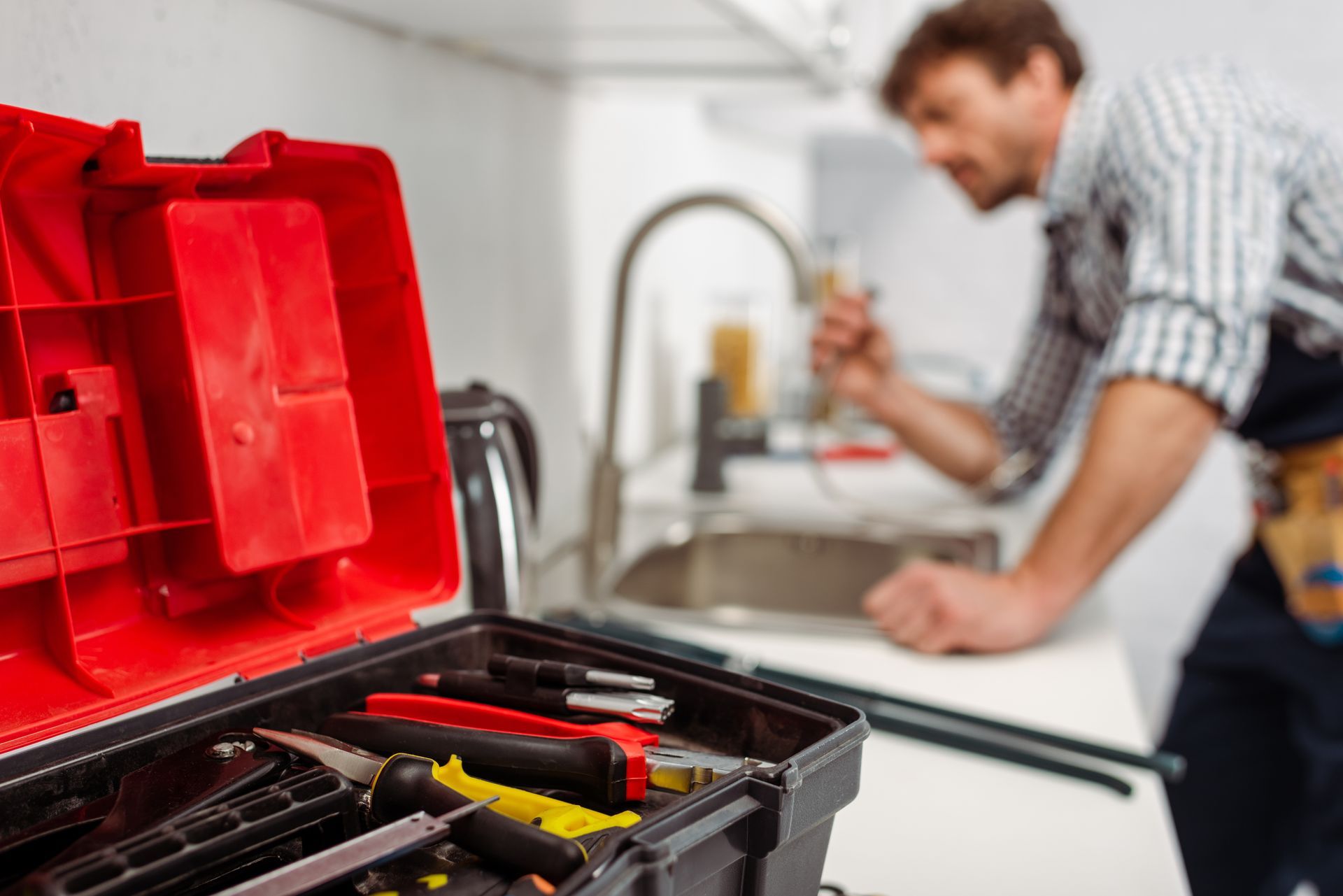 Open toolbox with plumbing tools as a technician works at a kitchen sink.