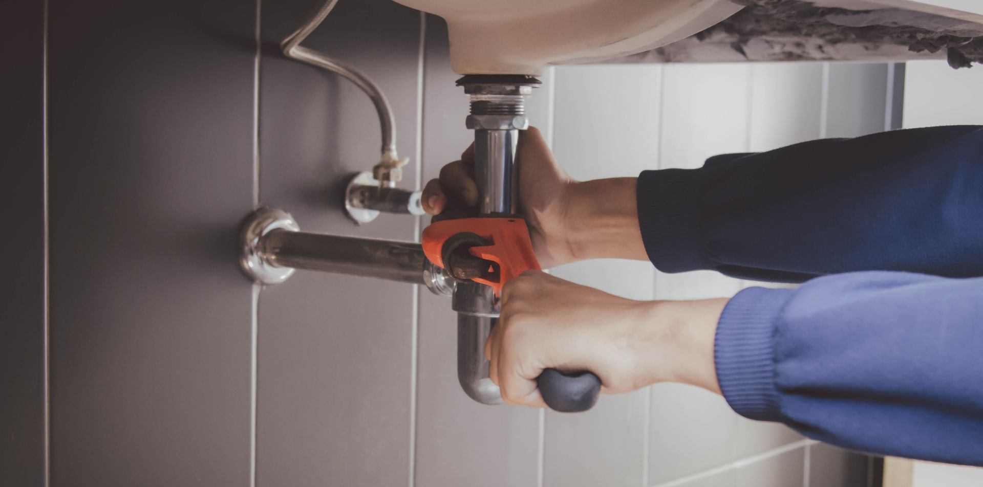 A professional plumber using a pipe wrench to repair a sink drain as part of a plumbing service A professional plumber using a pipe wrench to repair a sink drain as part of a plumbing service
