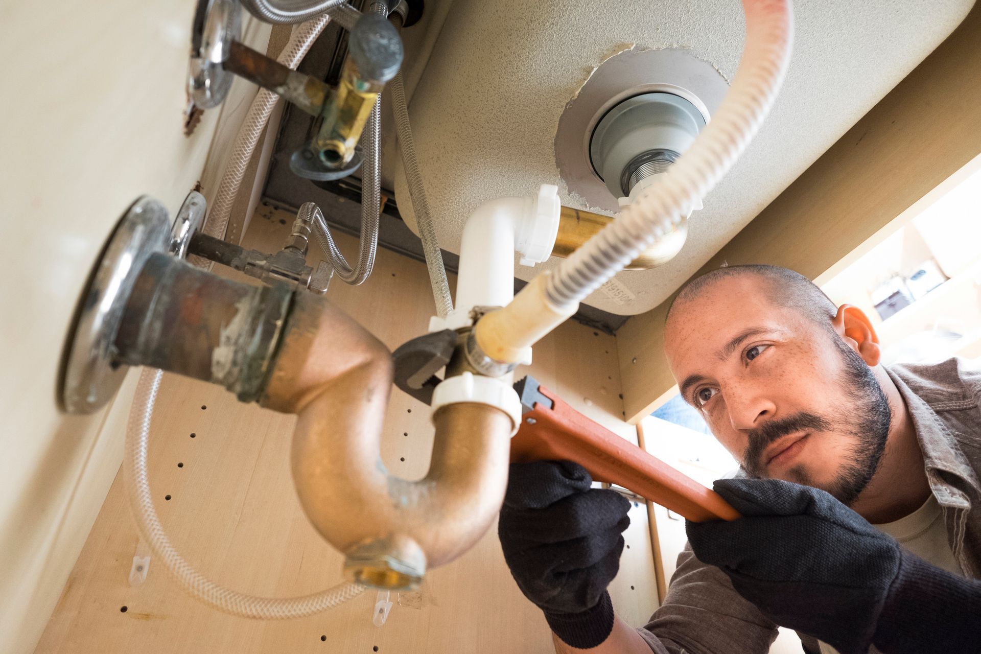 Plumber with a wrench fixing a sink's pipes under a bathroom cabinet.