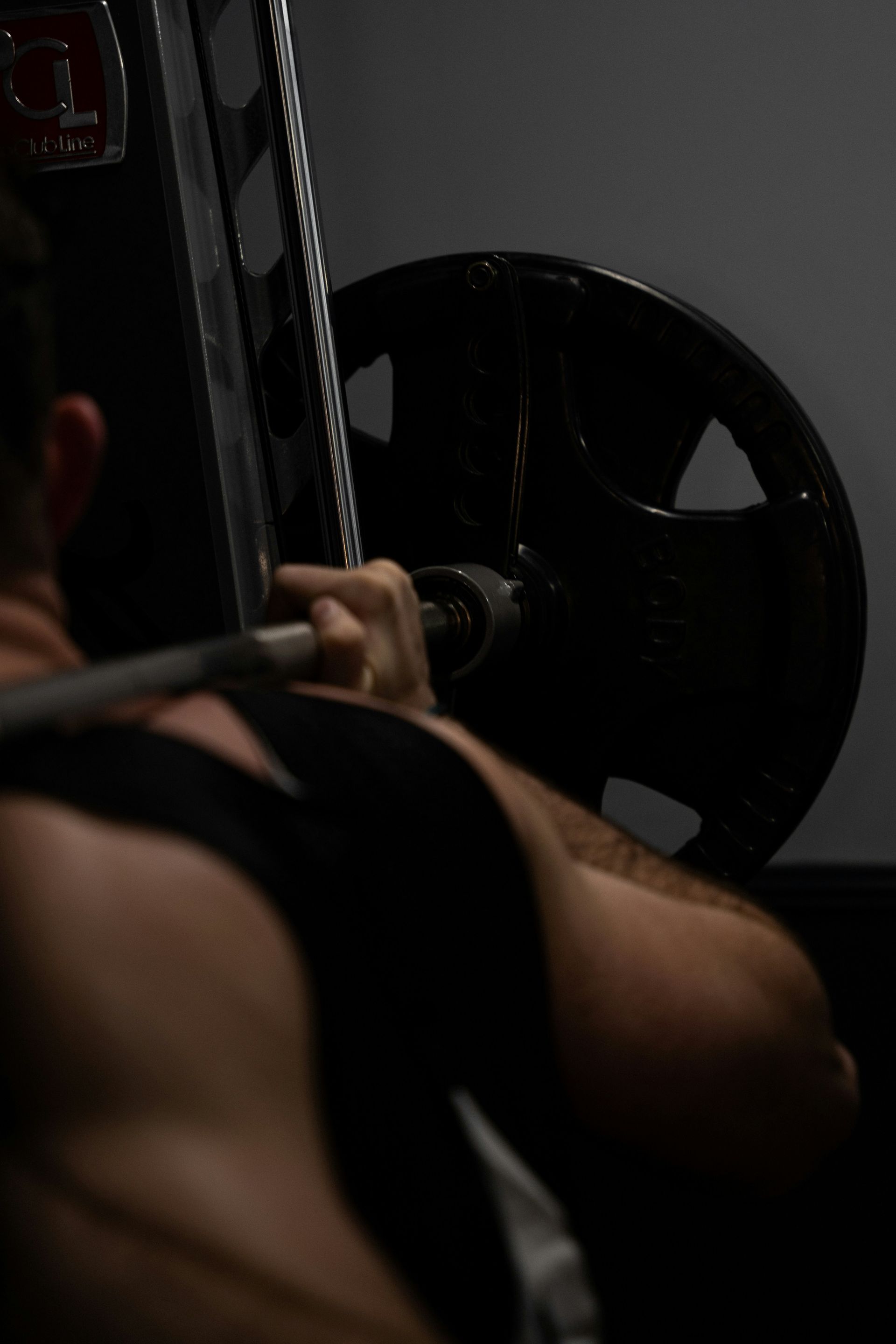 Person lifting a barbell in a dimly lit gym, with a large weight plate visible in the foreground.