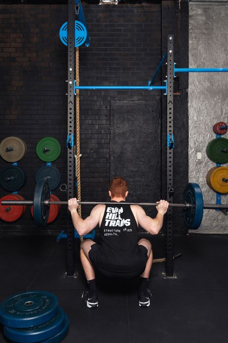 Person squatting with a barbell in a gym, surrounded by colorful weight plates.