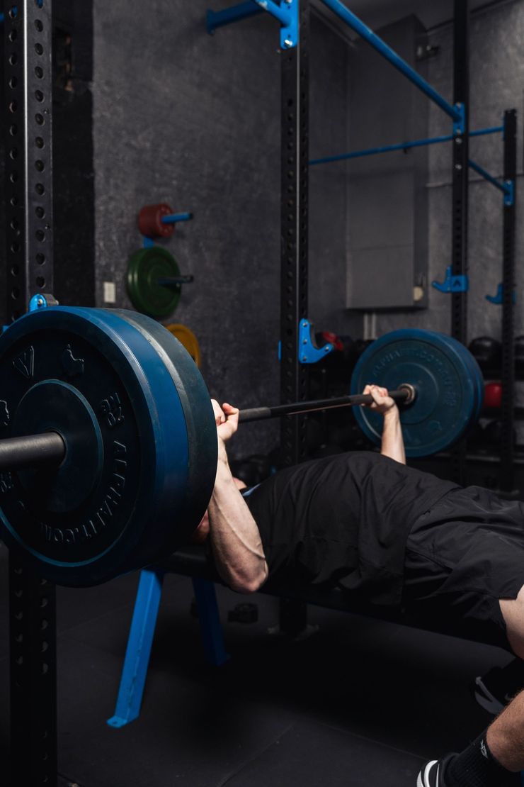 Person bench pressing a barbell with blue plates in a gym rack