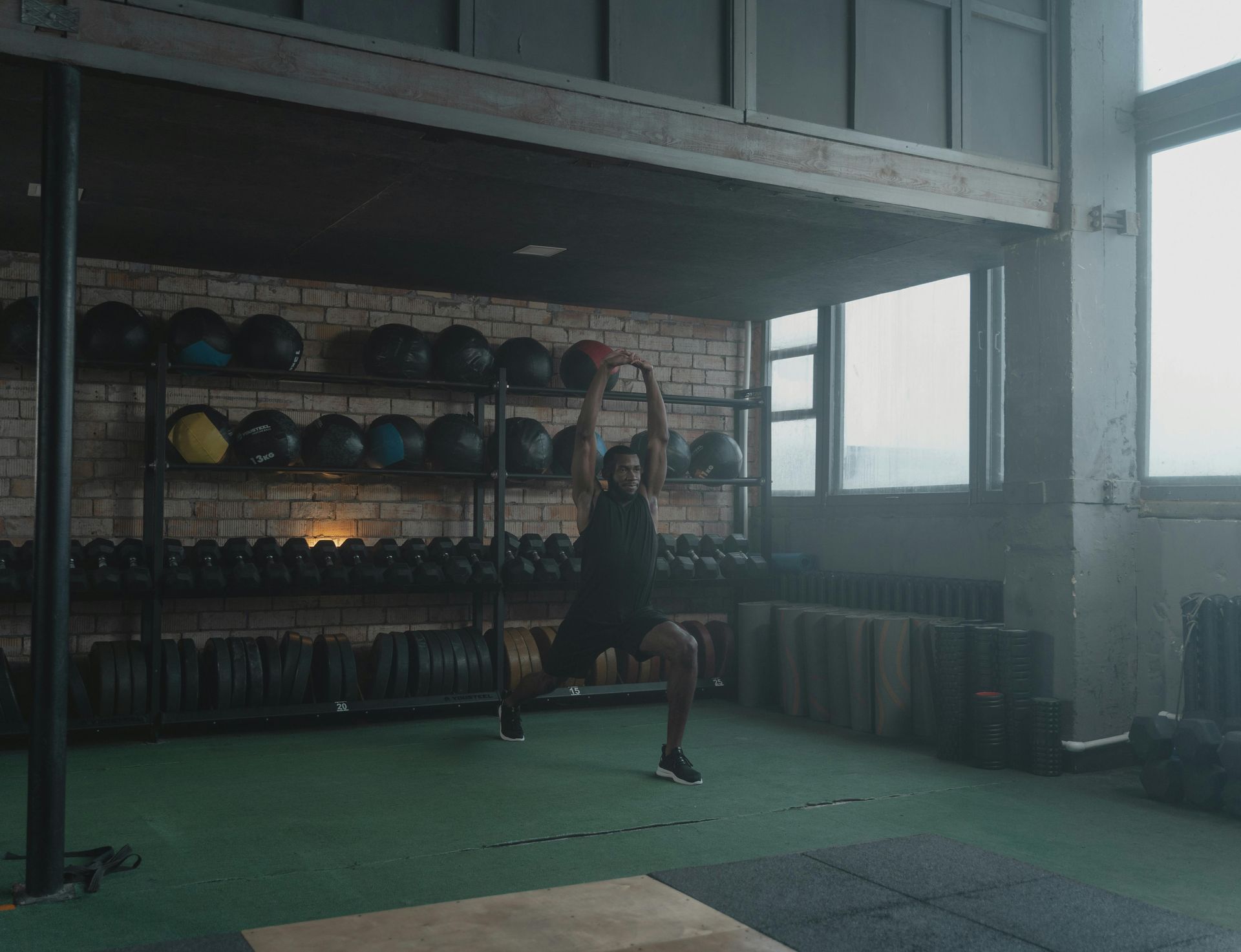 Person exercising in a dim gym, lunging on a green mat with weight racks in the background