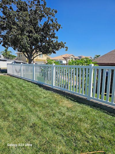 White fence along a grassy yard beside a tree under a clear blue sky