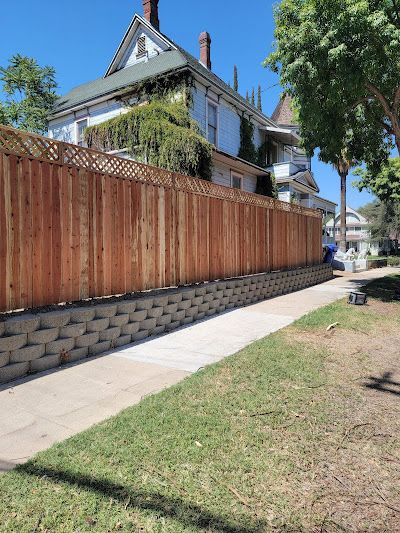 Victorian house behind a tall wooden fence beside a sidewalk on a sunny street
