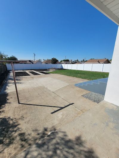 Backyard patio with concrete slabs, white fence, blue sky, and a blue tiled pool edge