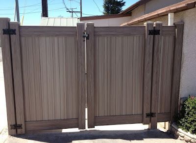 Tan wood privacy gate with dark metal hinges and latch between stucco walls in a sunny driveway