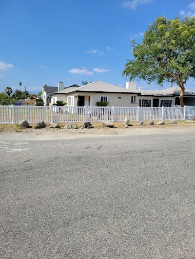 Single-story white house with a fenced yard and trees under a blue sky