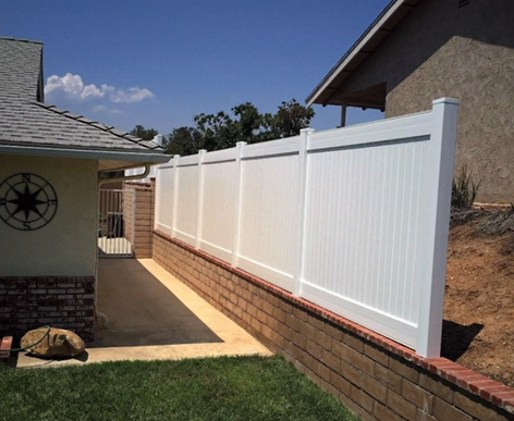 White privacy fence along a brick retaining wall beside a house walkway in a sunny yard