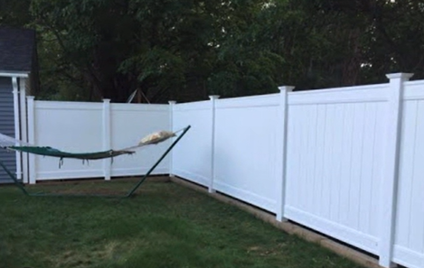 Backyard with a green hammock beside a white vinyl fence and trees in the background