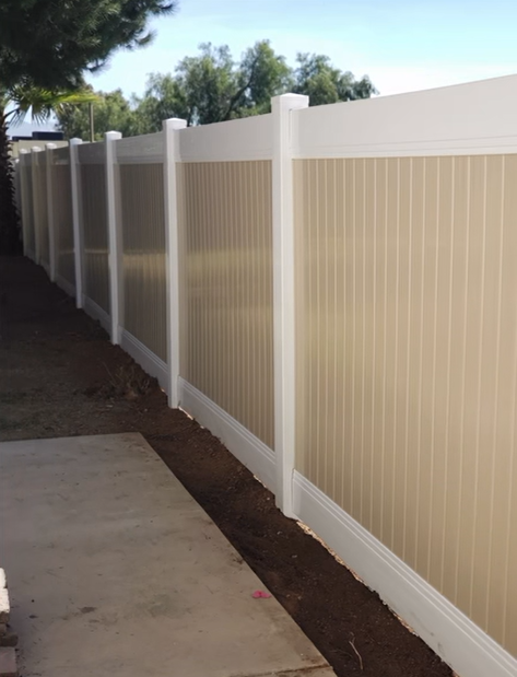 Beige vinyl privacy fence along a concrete walkway beside a house.