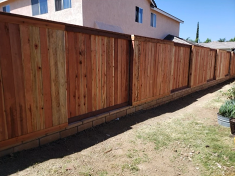 Wooden backyard fence with brick base beside a dry dirt yard and house