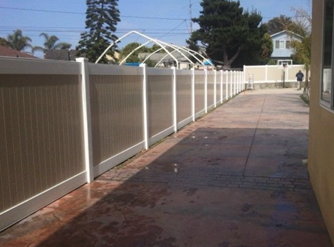 Long fenced driveway with a concrete path and white pergola frames in the distance