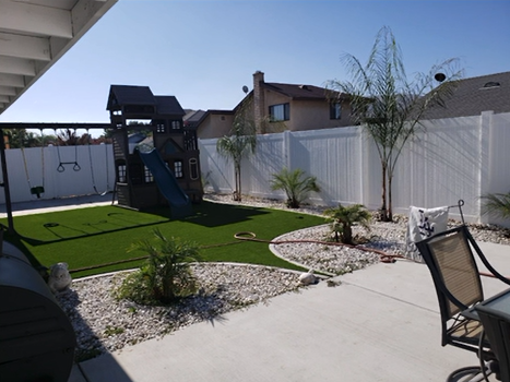 Backyard patio with artificial grass, white fence, and a small playset in bright sunlight