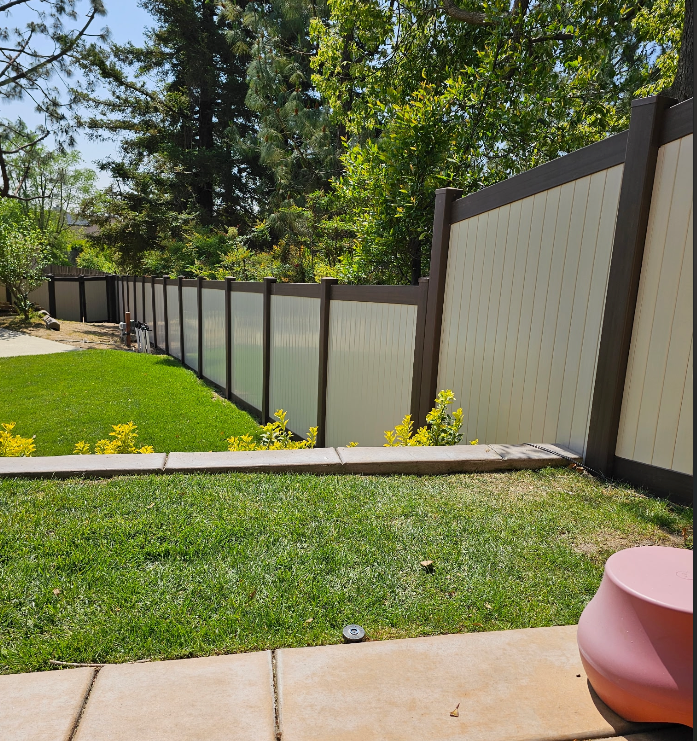 Backyard with green lawn, tan privacy fence, trees, and a patio edge in the foreground