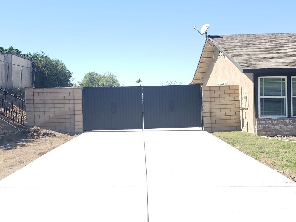 Driveway leading to a black double gate beside a beige house under a clear blue sky