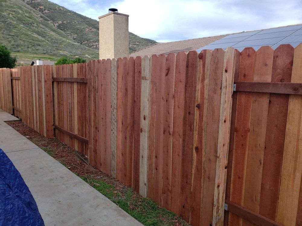 Wooden privacy fence along a narrow concrete path beside a hillside home