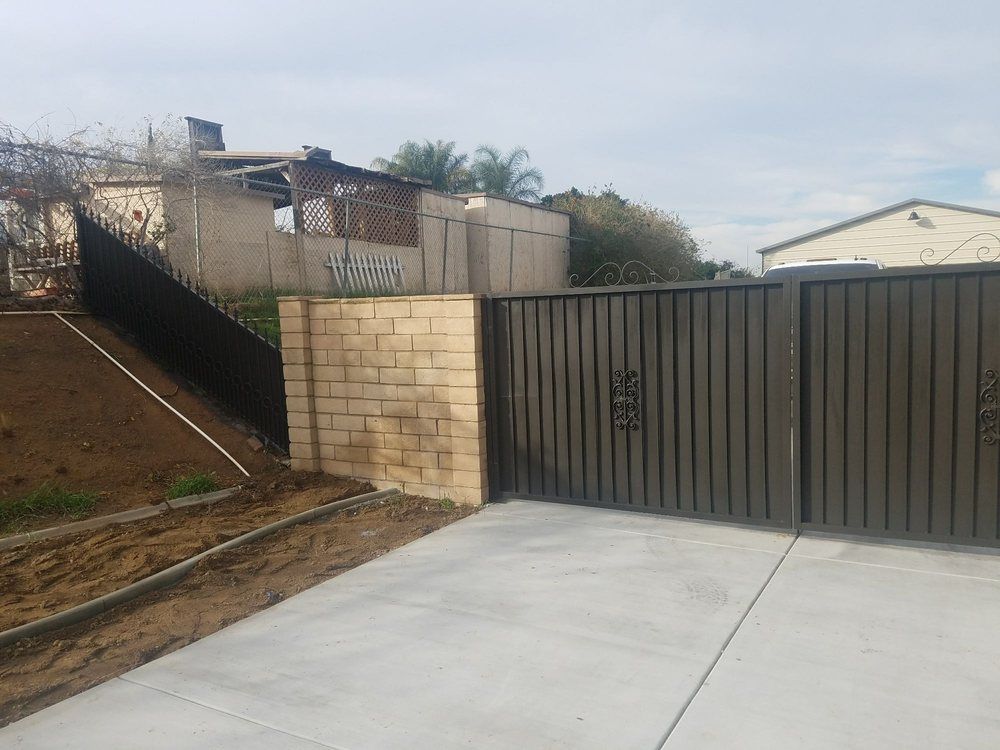 Concrete driveway with a gray metal gate and brick wall beside a sloped yard and house.