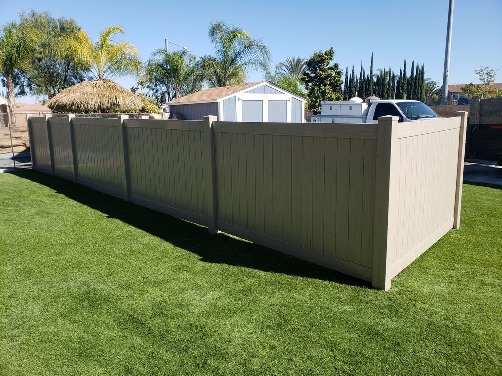 Tan vinyl fence enclosing a yard with green grass and a shed in the background