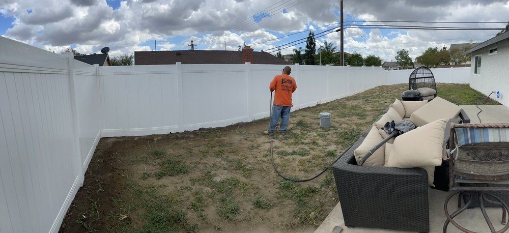 Backyard with white fence, cloudy sky, and a person in an orange shirt standing near patio furniture