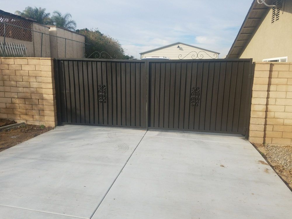 Closed black metal driveway gate with beige block walls and a concrete driveway.