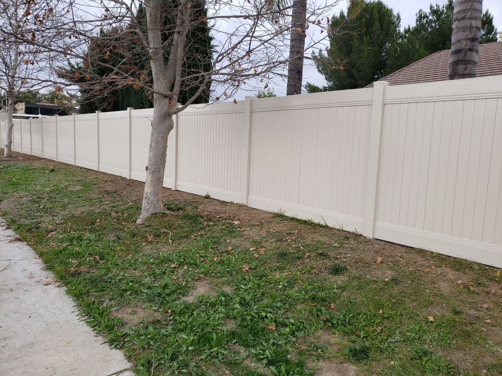 White vinyl fence along a sidewalk with leafless trees and patchy grass in a residential yard