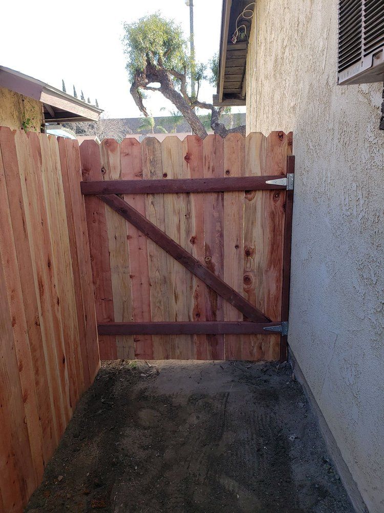 Narrow outdoor passage ending in a wooden gate between a stucco wall and wooden fence.