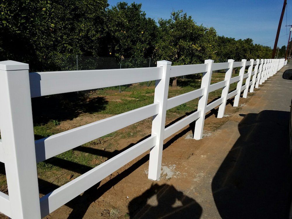 White wooden fence along a roadside with trees and grass in the background
