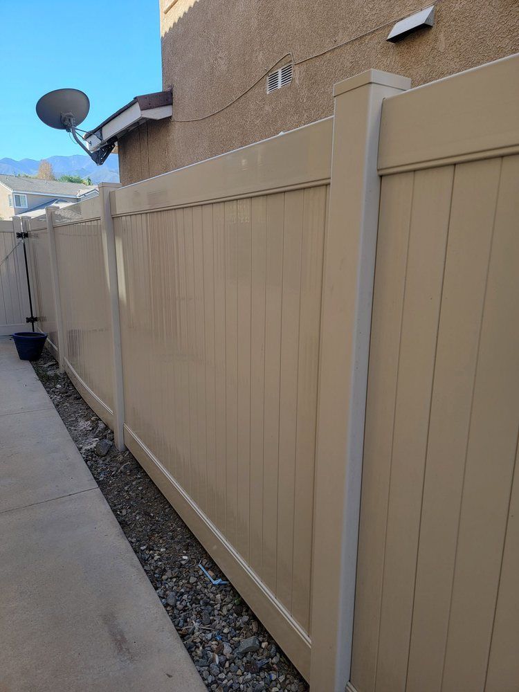 Narrow side yard with beige vinyl fence beside a concrete walkway and gravel strip along a stucco house.